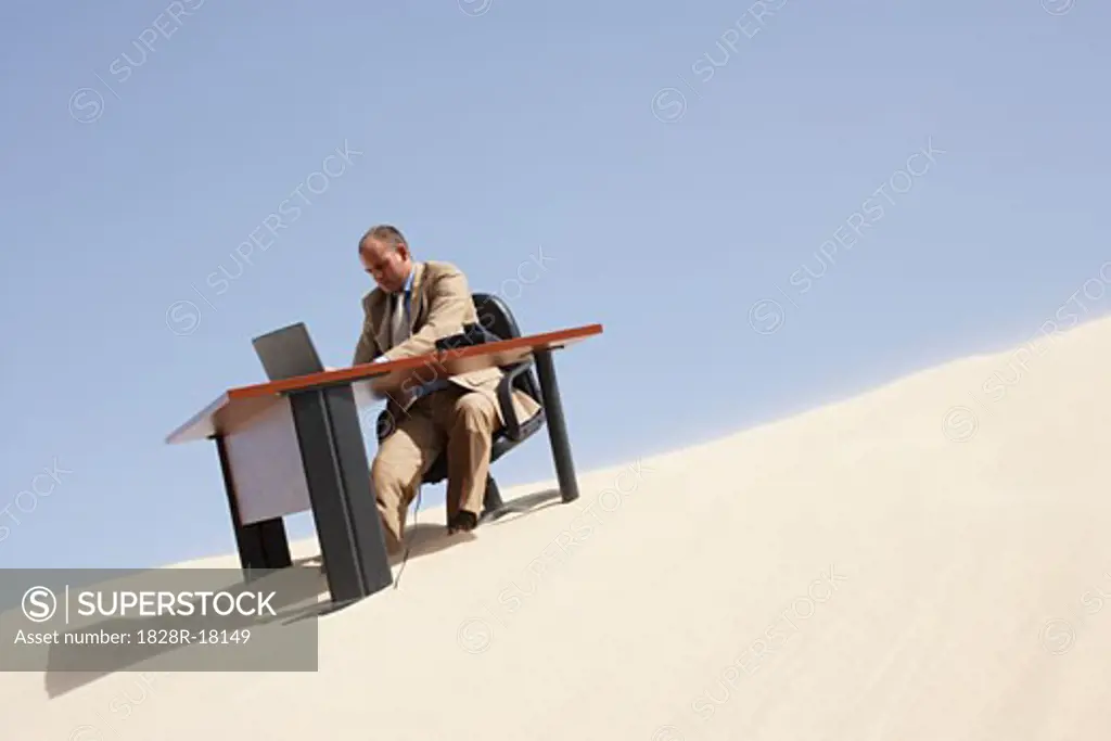 Businessman at Desk at Top of Sand Dune   