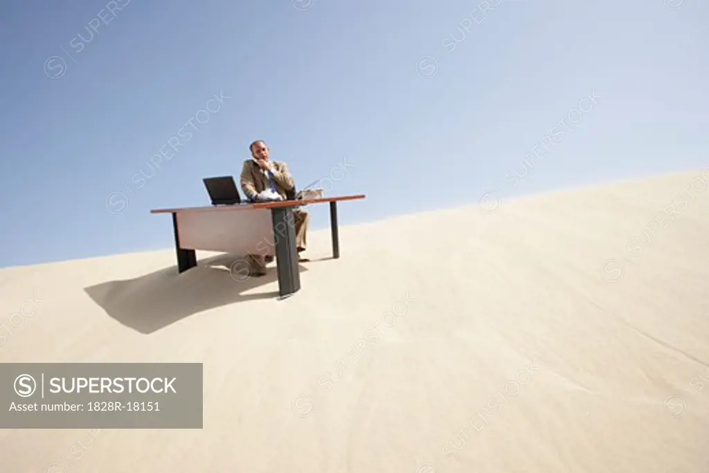 Businessman at Desk at Top of Sand Dune   