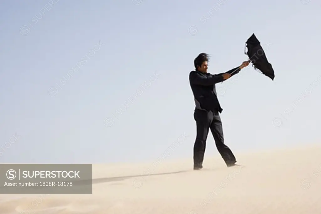 Businessman in Desert with Windswept Umbrella   