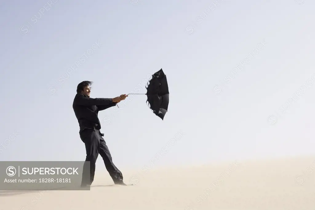 Businessman in Desert with Windswept Umbrella   