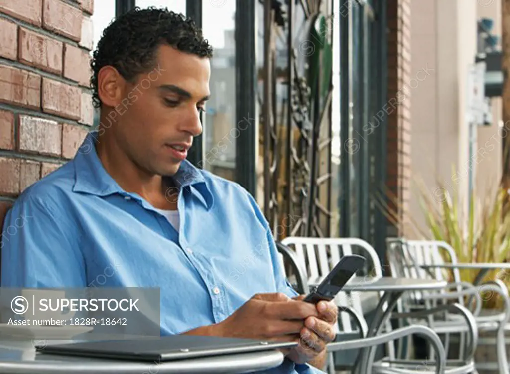 Man sitting at Cafe Table and Using Cellular Phone   