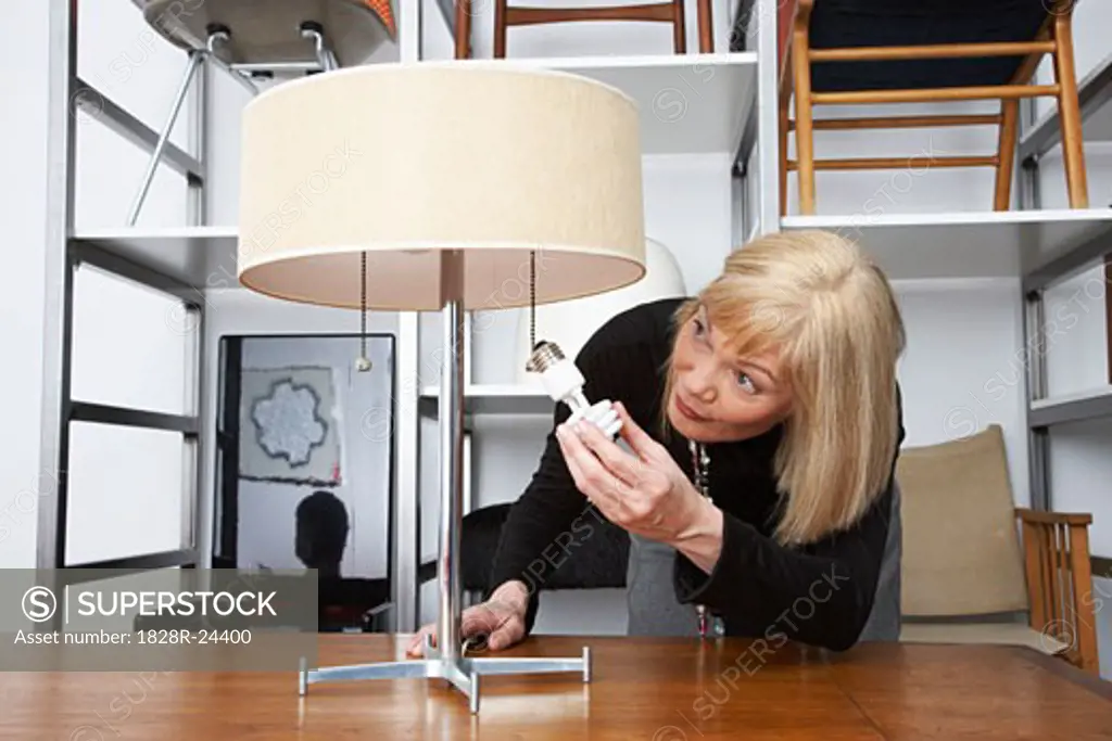 Woman Putting Lightbulb in Lamp in Furniture Store   