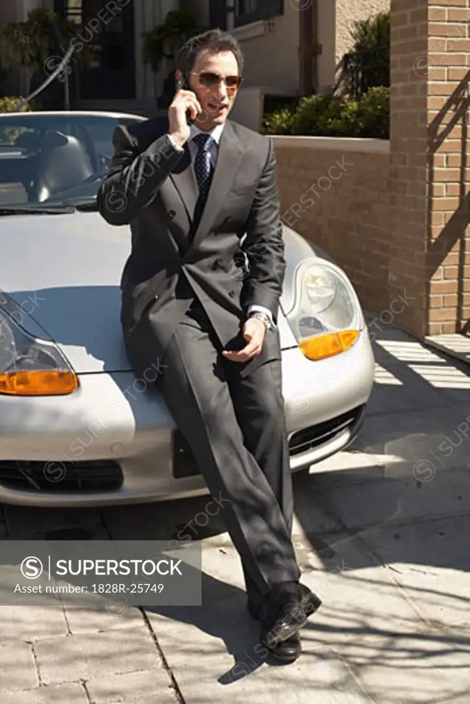 Businessman with Cellular Phone Leaning on Car   