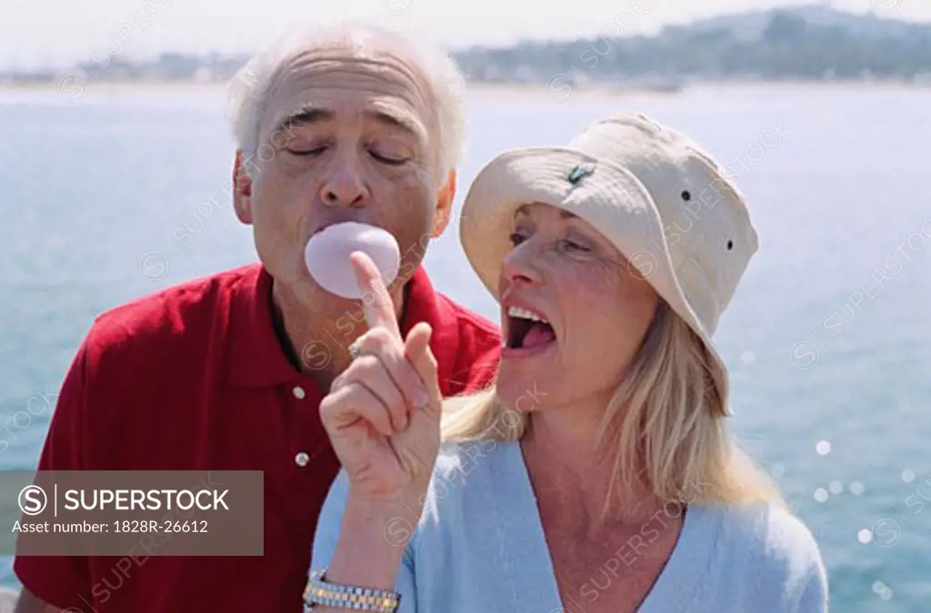 Man Blowing Bubble Gum, woman Trying to Burst Bubble   