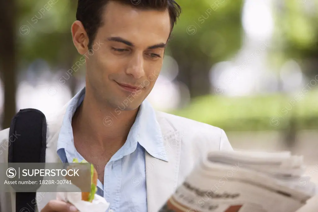 Man Eating Sandwich and Reading Newspaper   