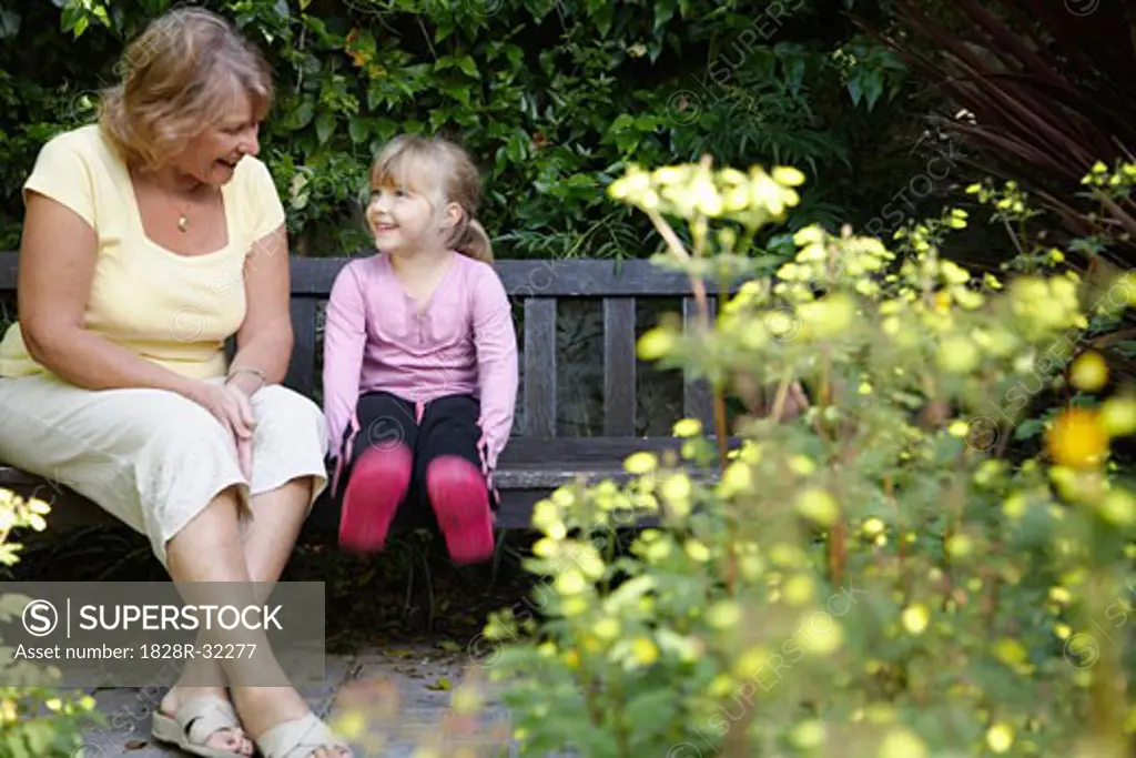 Grandmother and Granddaughter Sitting on Bench in Garden   