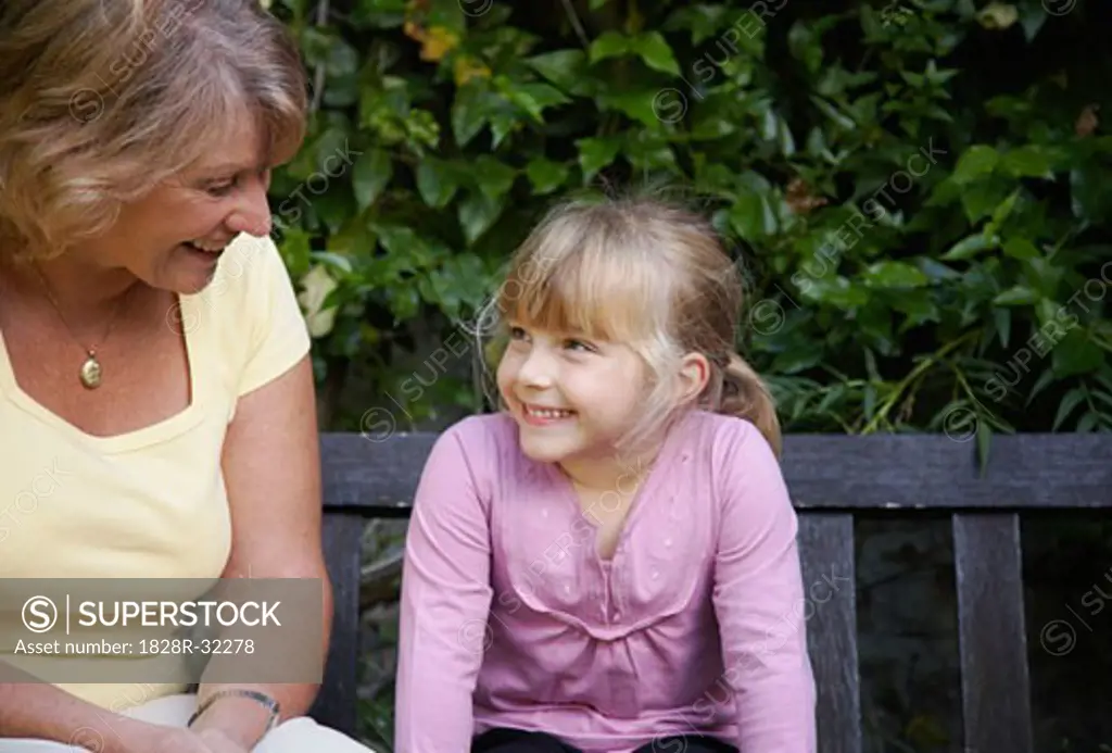 Grandmother and Granddaughter Sitting on Bench in Garden   