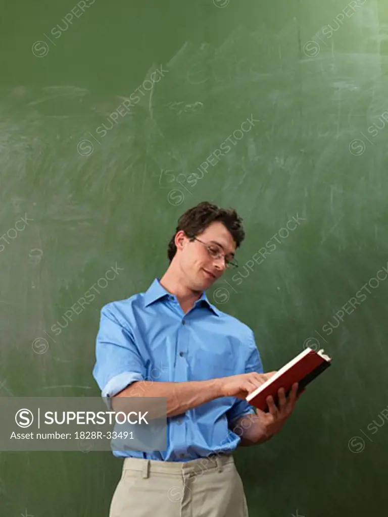 Teacher with Book in Front of Blackboard   