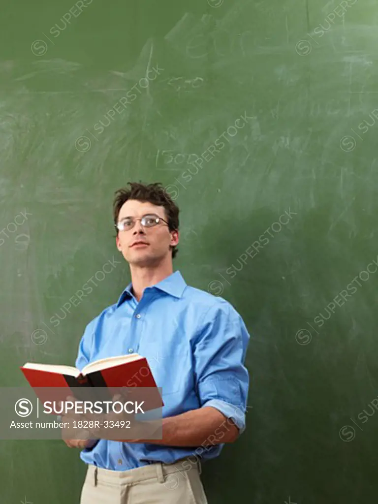 Teacher with Book in Front of Blackboard   