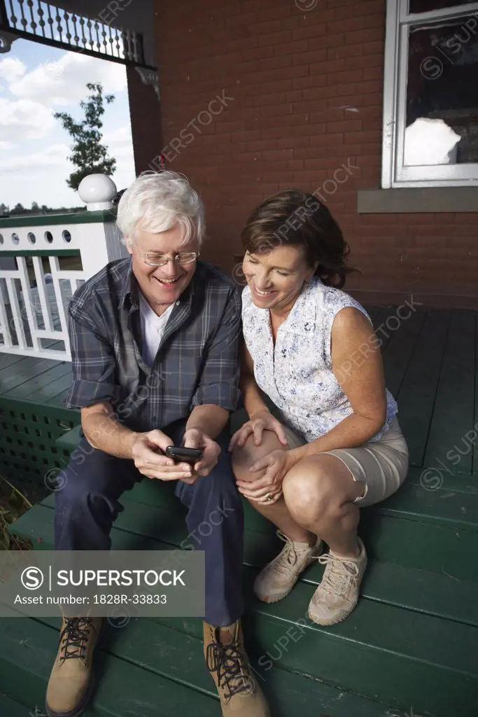 Couple with Electronic Organizer on Porch of Farmhouse   