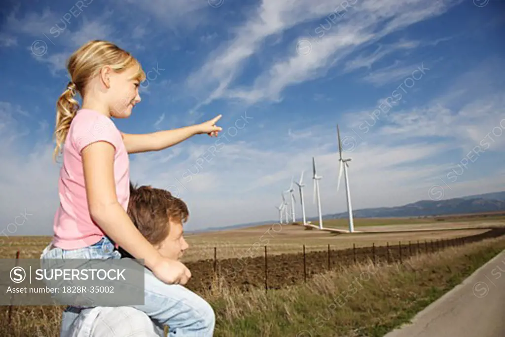 Young Girl on Father's Shoulders Pointing at Wind Turbines   