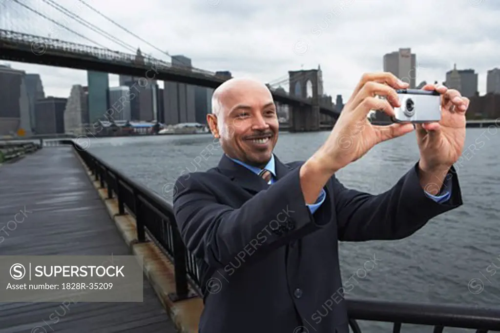 Businessman taking Self Portrait by Brooklyn Bridge, New York City, New York, USA   