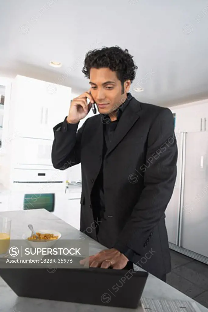 Businessman at Home, Using Laptop Computer and Talking on Cell Phone   