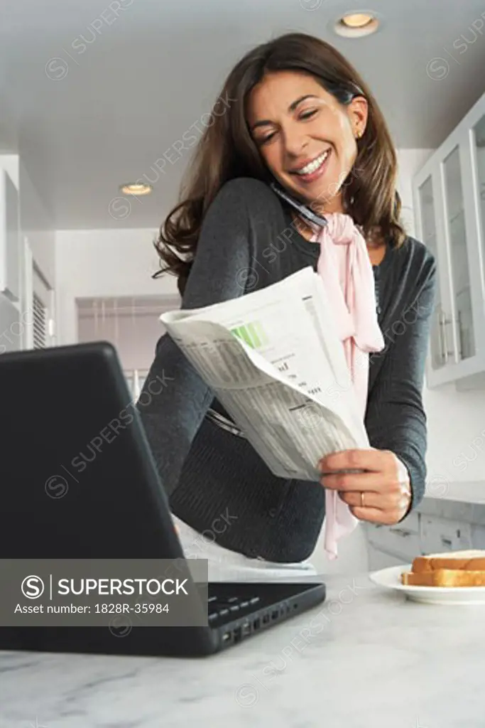 Businesswoman at Home, Using Laptop Computer and Talking on Cell Phone   