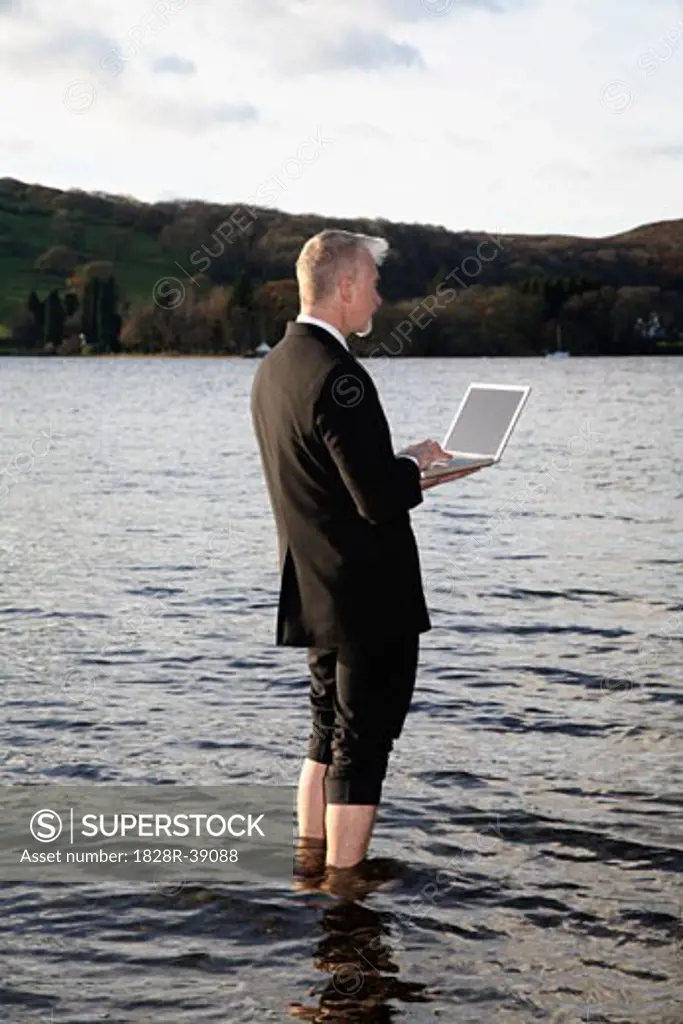 Businessman with Laptop Computer Standing in Lake Windermere, Cumbria, England   
