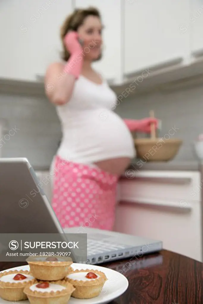 Pregnant Woman Baking in Kitchen with Laptop Computer   