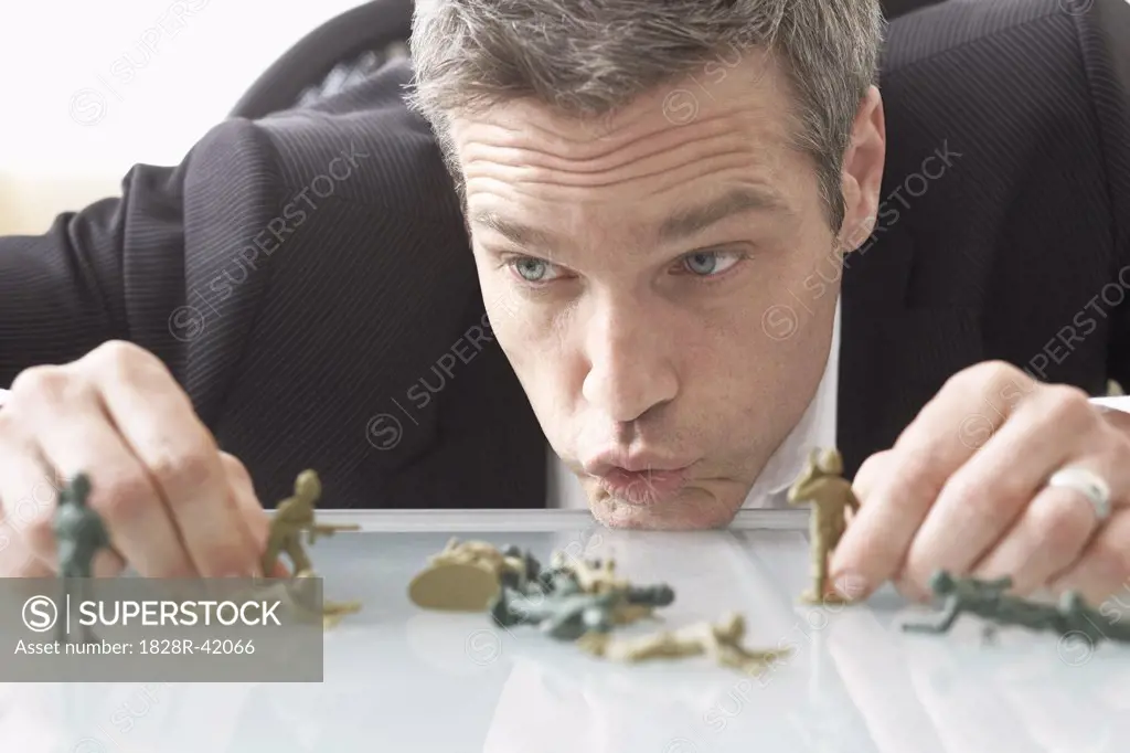 Businessman Playing with Toy Soldiers on Desk   