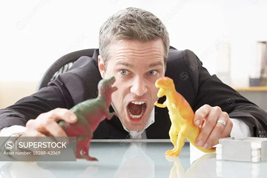 Businessman Playing with Toy Dinosaurs on Desk   
