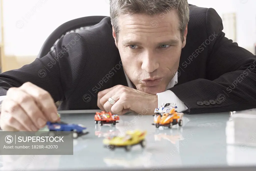 Businessman Playing with Toy Race Cars on Desk   