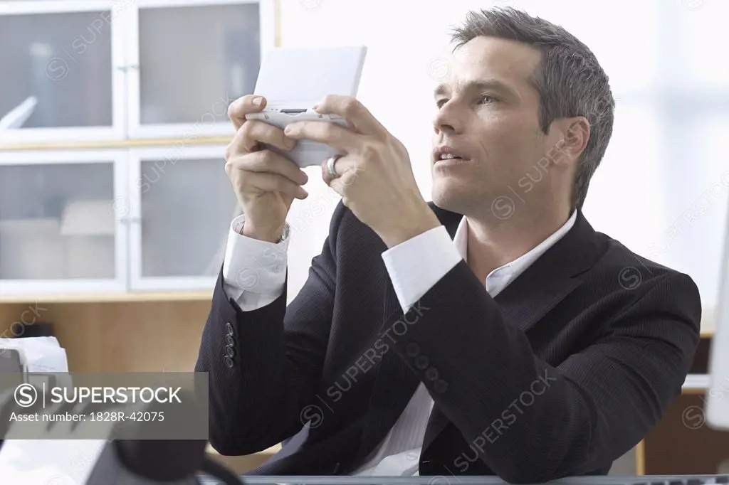 Businessman Playing Handheld Video Game at Desk   