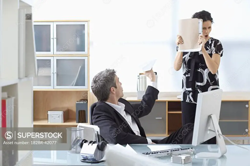 Businessman Throwing Paper Airplane at Businesswoman in Office   