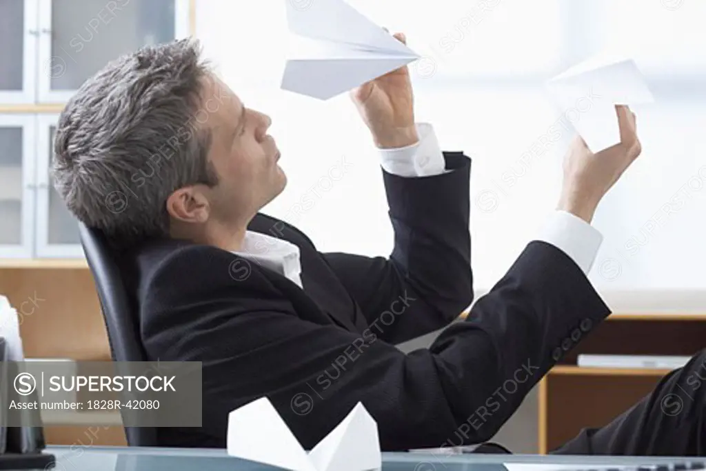 Businessman Playing with Paper Airplanes at Desk   