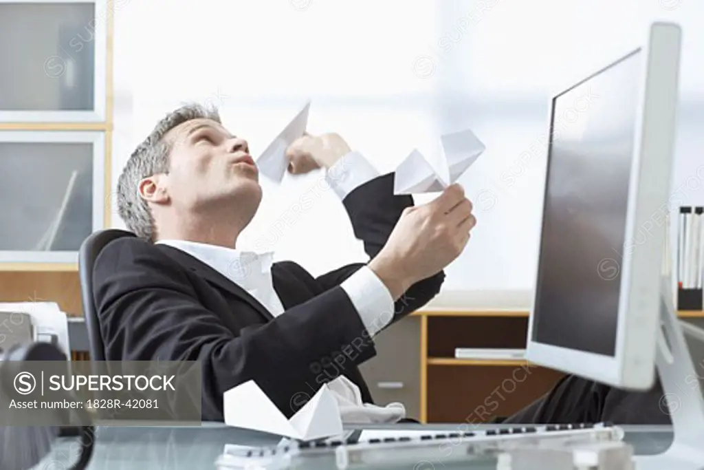 Businessman Playing with Paper Airplanes at Desk   