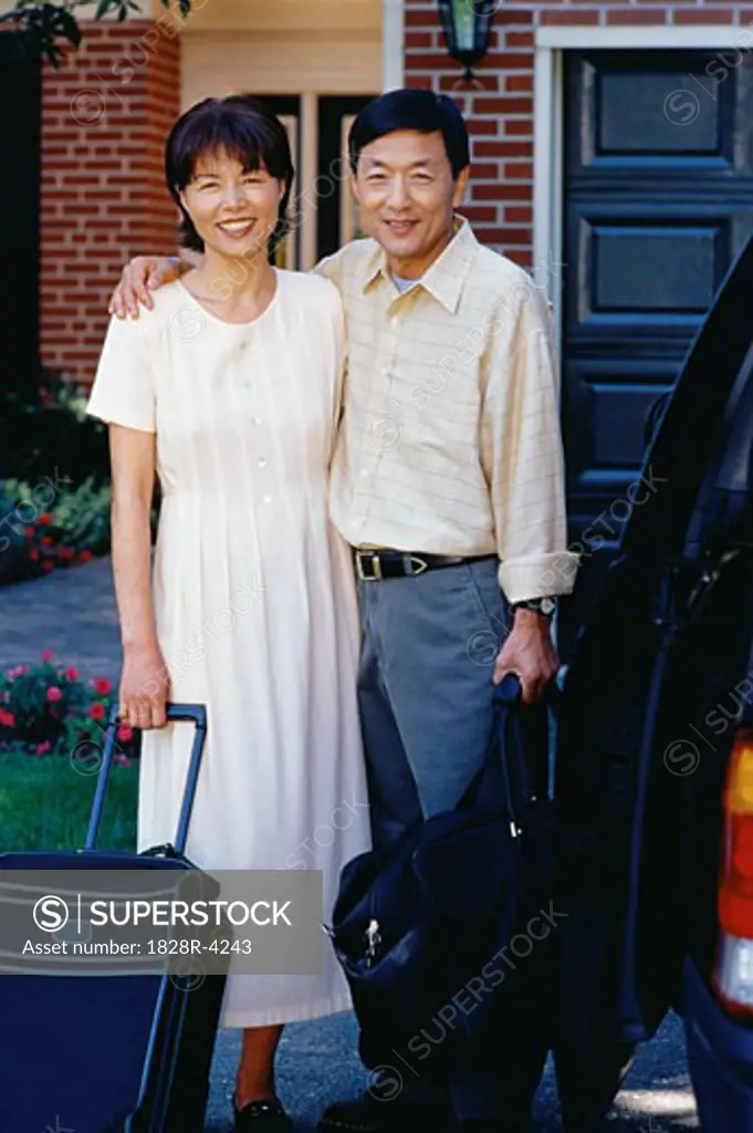 Portrait of Mature Couple in Front of House with Luggage   