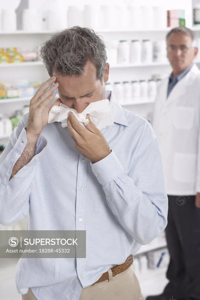 Man in Pharmacy Blowing Nose, Pharmacist in the Background   