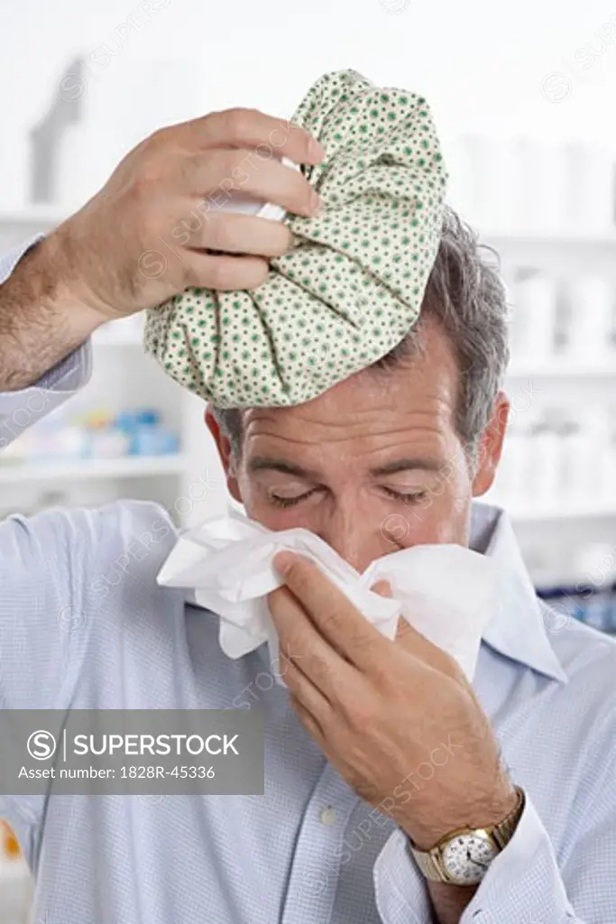 Man in Pharmacy Blowing Nose, Holding Ice Pack on Head   