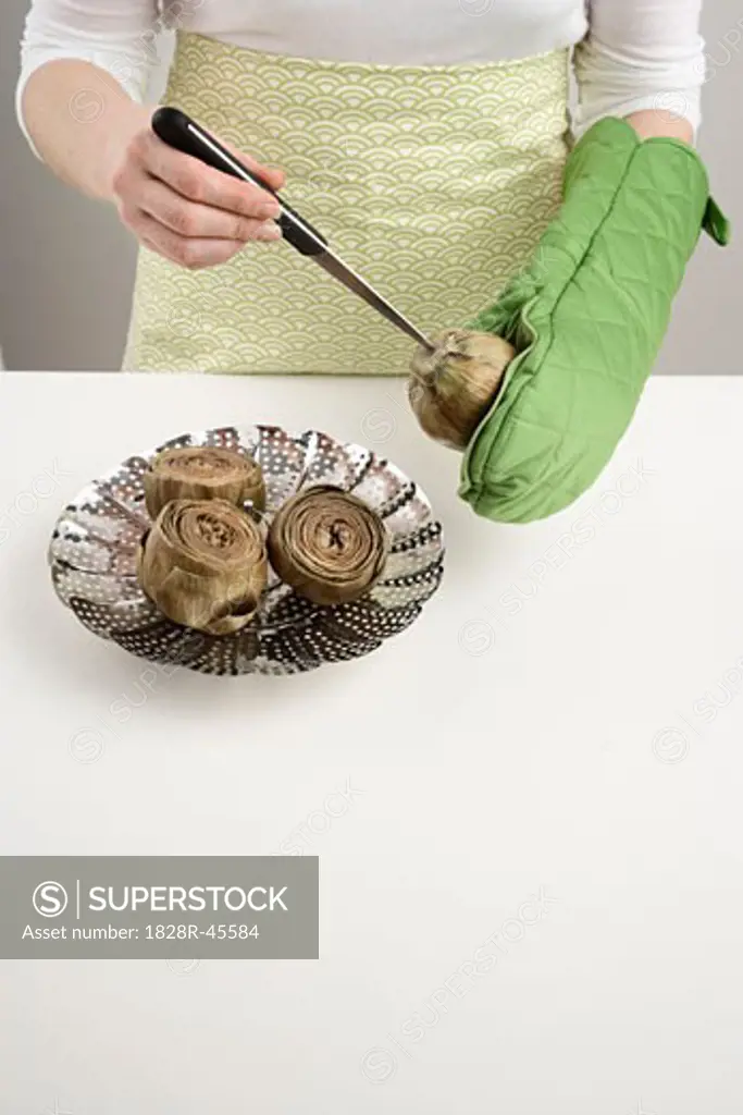 Woman Using a Knife to Check if Artichokes Are Ready   