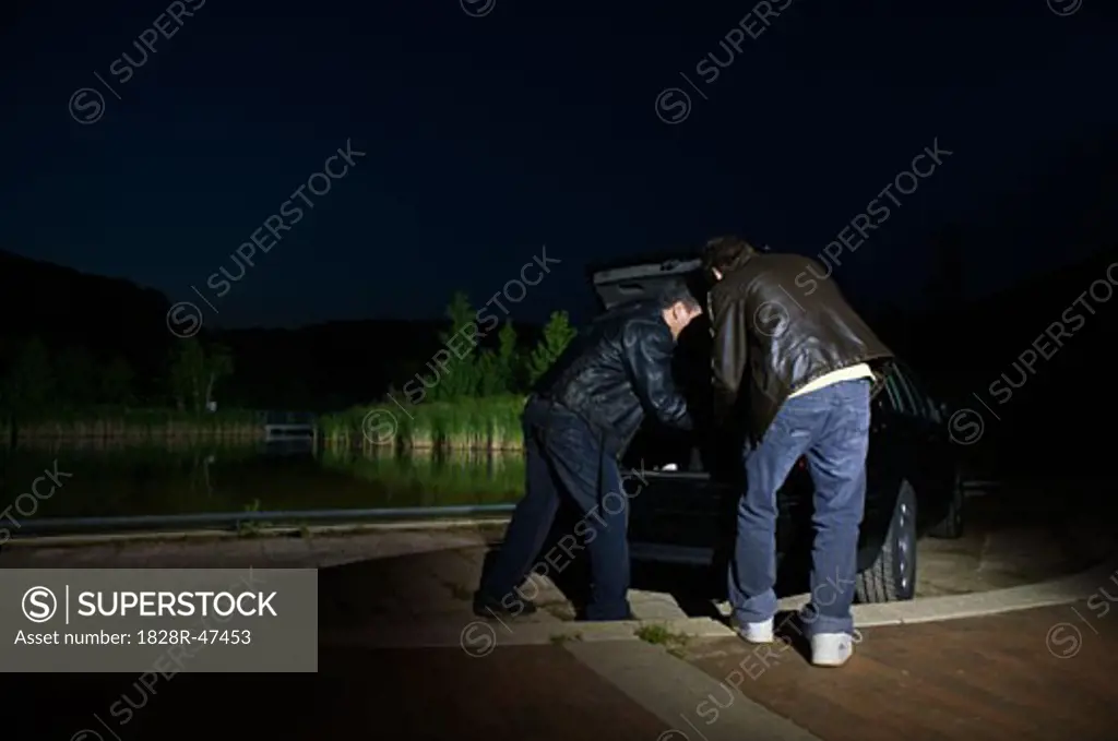 Men Removing Something From Car Trunk at Night   