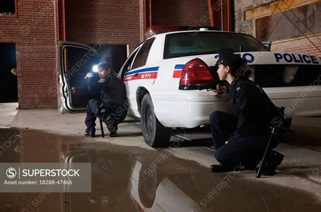 Police Officers Crouching Behind Police Car With Guns Drawn   