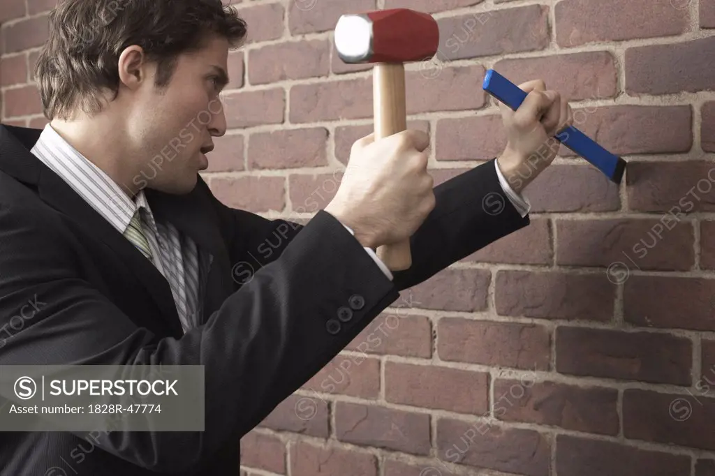 Businessman using Mallet and Chisel on Brick Wall   