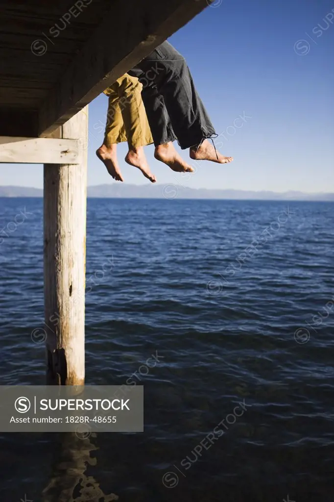 Women Dangling Feet from Dock over Lake   