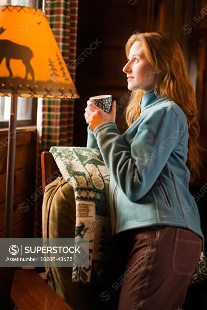 Woman With a Cup of Cocoa Looking Out Window of Cabin   