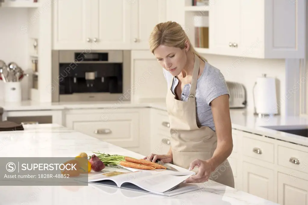 Woman Reading Cookbook in Kitchen   