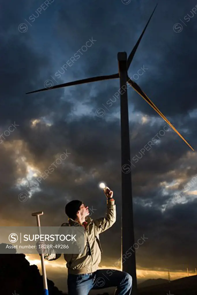Man Holding Lightbulb by Wind Turbine   