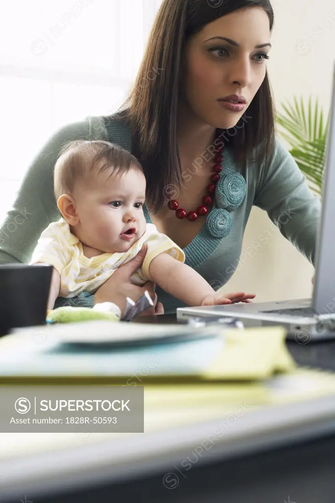Mother Using Laptop Computer With Baby on Her Lap   