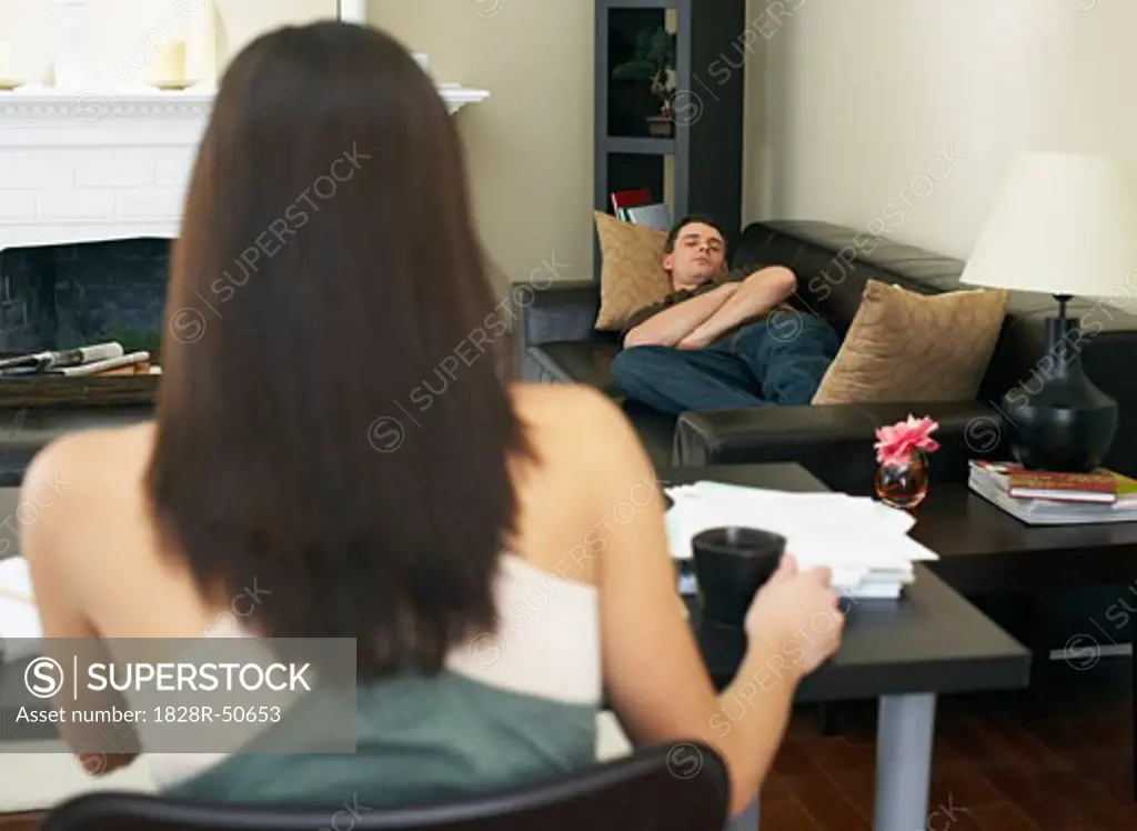 Woman Working at Computer and Man Napping on Couch   