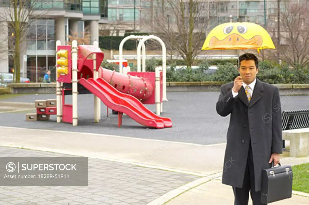 Businessman With Child's Umbrella In Playground   