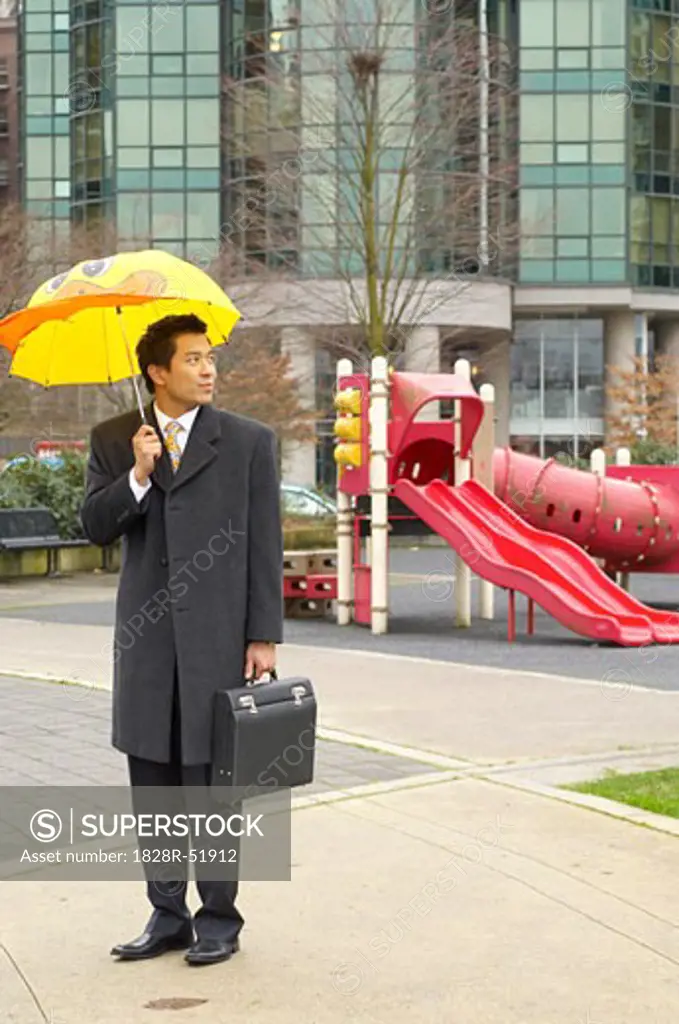 Businessman With Child's Umbrella In Playground   