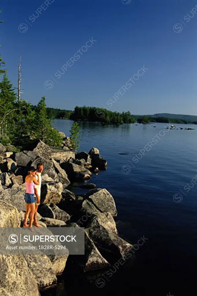 Couple Standing on Rocks near Lake, Belgrade Lakes, Maine, USA   