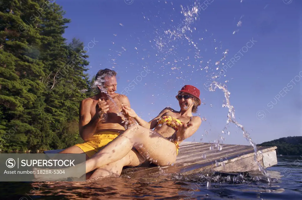 Couple in Swimwear on Dock Splashing Water, Belgrade Lakes, Maine, USA   