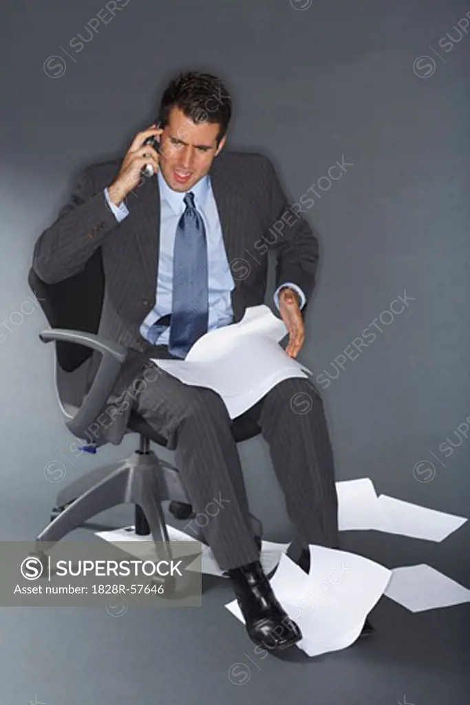 Angry Businessman Talking on Cell Phone Surrounded by Documents   