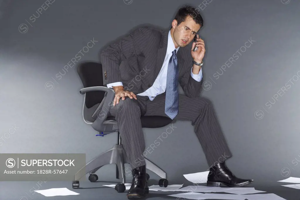 Angry Businessman Talking on Cell Phone Surrounded by Documents   