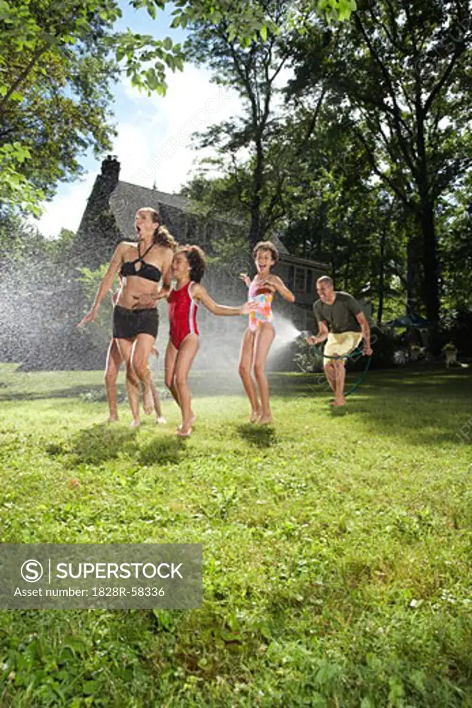 Family playing in backyard with sprinkler   