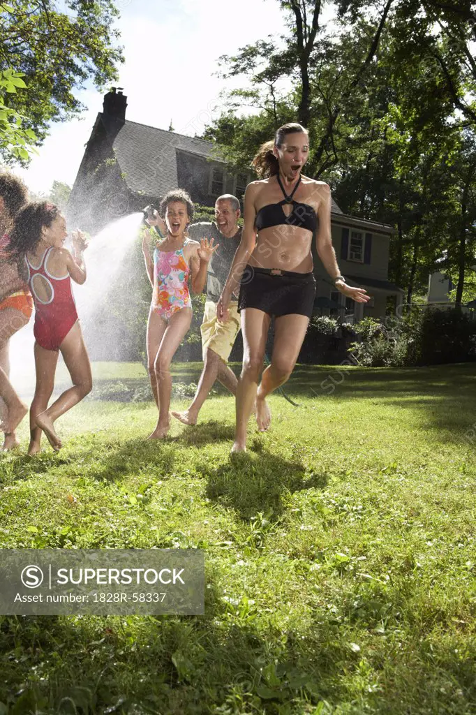 Family playing in backyard with sprinkler   