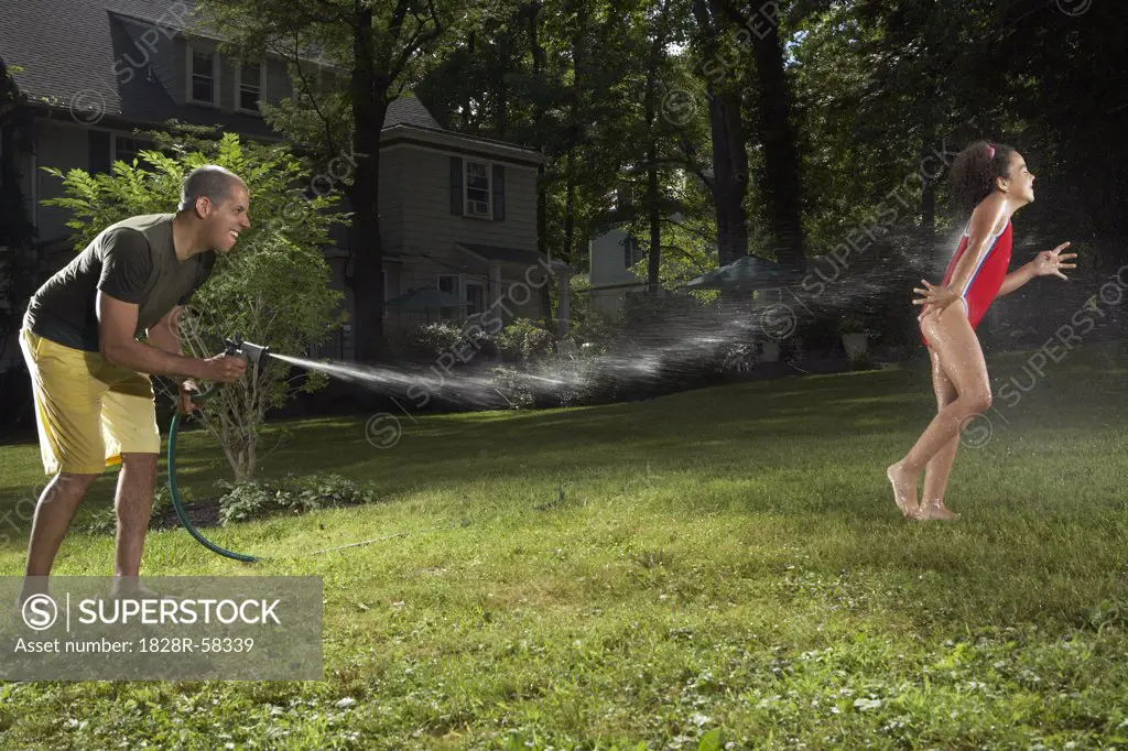 Father and Daughter Playing with Water Hose in Backyard   