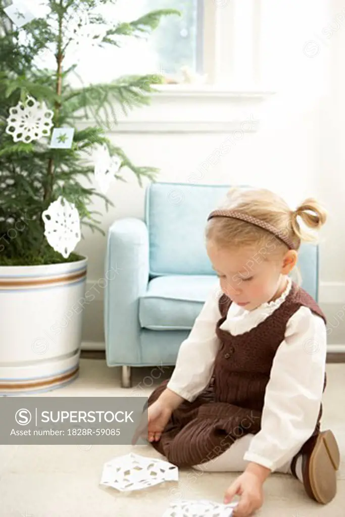 Little Girl Decorating a Christmas Tree With Paper Snowflakes   